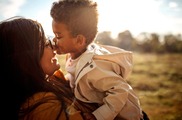 Woman of color holding up in her arms toddler of color.