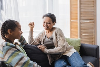 smiling african american woman talking with teenage daughter on couch at home