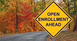 Caution Road sign, "Open Enrollment Ahead." on a curvy road with trees losing their leaves.