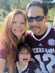 Photo of Nicole Anzaldua, her husband and toddler son, smiling at the camera, in sunny park-like surroundings.