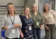 Four women stand in row smiling.