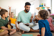 Man with dark hair sits in classroom and teaches children.