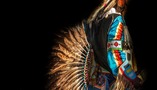 Photo of a Native American wearing ceremonial dressing in dramatic lighting. 