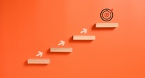 Bright orange background with wooden steps, bullseye at top step with arrows pointing to the top step.