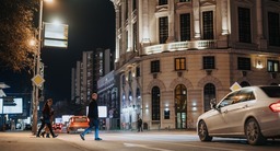 City scape with people using well-lit crosswalk and cars stopped for pedestrians. 