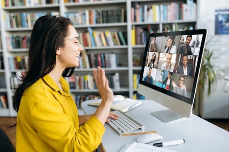 Woman in yellow blouse smiling and greeting other individuals on virtual meeting like her. 