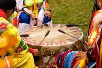 Close up of three Native Americans in Native regalia in drum circle.