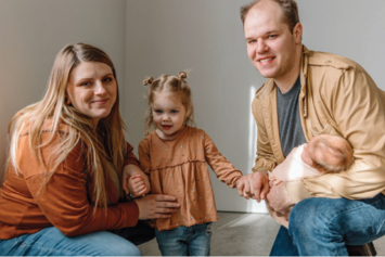 Photo of Michelle Troxler next to her toddler daughter and her husband holding their baby daughter.