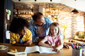 Father helping children with homework in kitchen