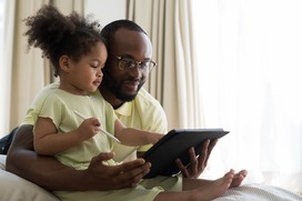 Dad and young daughter holding a stylus look at a tablet together.