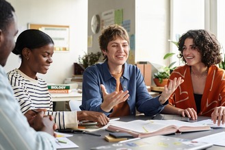 Teacher interacting with diverse group of engaged students during study session around table, with books