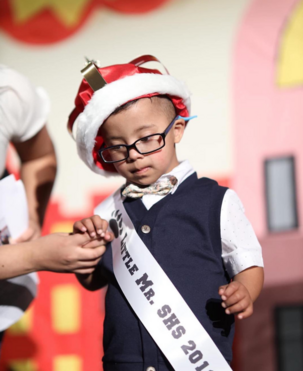 boy winning a pageant wearing glasses and a king crown