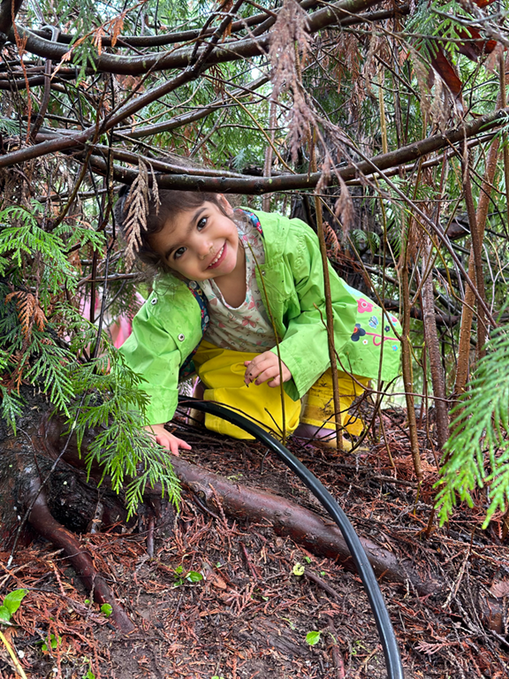 Young girl wearing jacket peaks out through tree limbs.