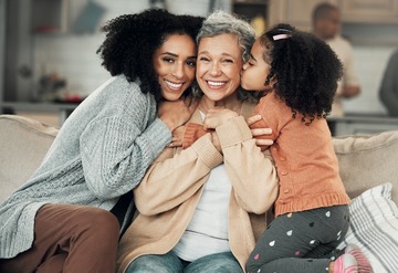 Kiss, portrait and grandmother with girl and woman on a sofa, hug and happy in their home together.