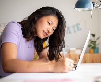 Asian female college student doing homework writing on paper at home. 