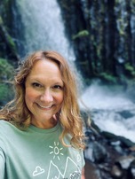 Medium shot of Kerianne Christie, smiling, standing in nature in a front of a waterfall.