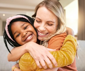 Portrait, family and adoption with a girl and mother hugging in a living room of their house together.