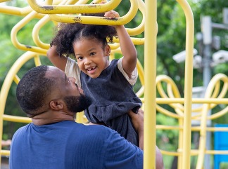 Black man, father carrying little daughter playing at playground in the park