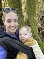 Photo of Shannon Wilcox holding her toddler son, both smiling, in a forest setting.