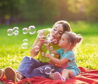 Family in park -Female child blows soup foam and make bubbles with her mother in nature.