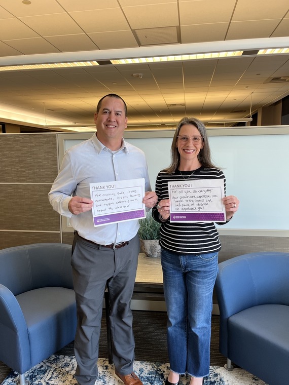Man and woman stand side by side holding squares of papers with messages on them.