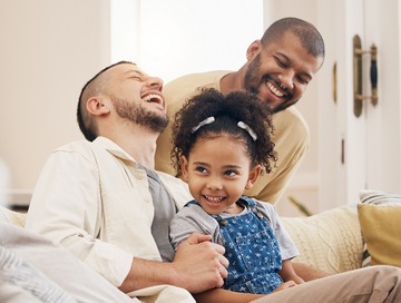 couple, male, laughing with their child on a sofa in their home 