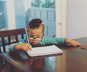 boy with down syndrome at a table with glasses on writing on a paper