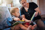 A mother and her toddler son sit together reading a book.