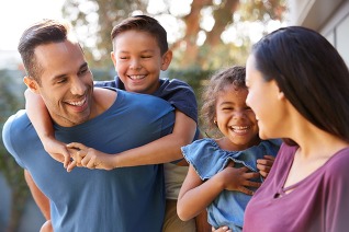 family outside smiling, son on dads back, mom holding daughter