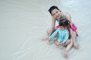 Woman with young girl sitting in shallow open water outside.