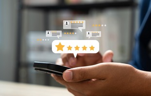 photo of a hand holding a smart phone, above smart phone are stars and the icons for different reviews people have given online. 