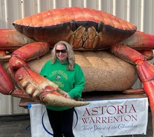 Vanessa Hagerty, smiling and holding a giant claw of an inflatable red crab, next to a sign reading, “Astoria Warrington, the Spirit of the Columbia.”