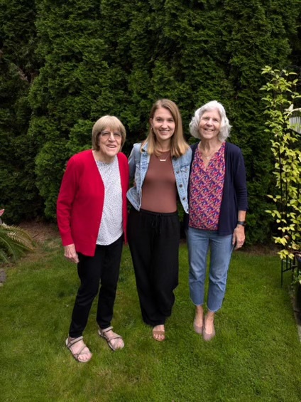 Three women stand side-by-side on grass.