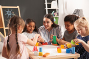 Woman sitting at table with children playing and learning.
