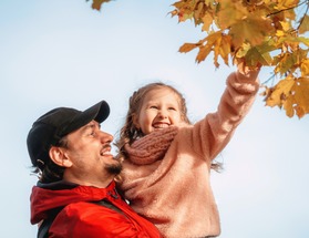 Dad and daughter hug, play and laugh on an autumn walk. A girl hugs her parent touching a branch of colorful autumn maple leaves. 