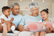 Older man and woman sit with young children and read to them from a book.