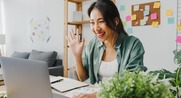 Woman sitting at desk looking at computer screen, raising hand.