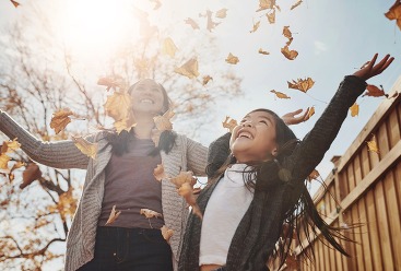 Autumn, mother and daughter throwing leaves in garden of home together