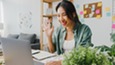 Woman sitting at desk looking at computer screen, raising hand.