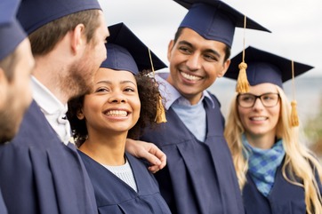 students smiling with graduation caps on outside 