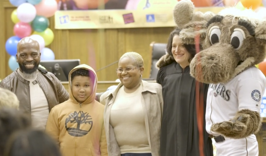family of three smiling with judge and mariners mascot celebrating their adoption finalization