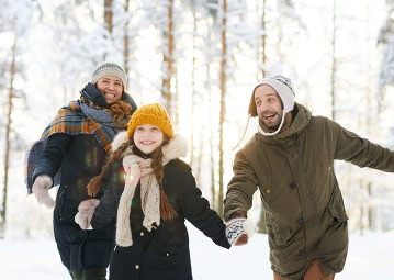 Portrait of playful family running in winter forest all smiling happily in sunlight