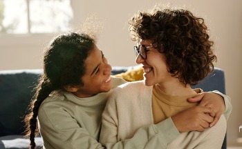 African American happy teenage girl embracing her foster mom while they spending time together at home