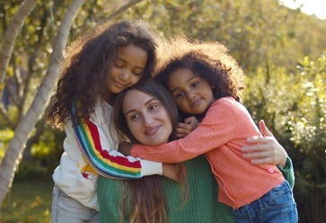 young mom anddaughters hugging in park