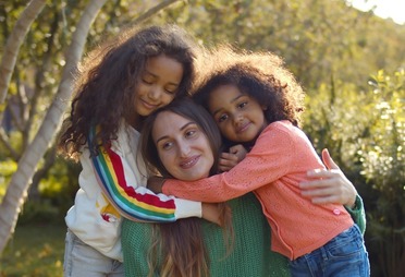 young mom anddaughters hugging in park