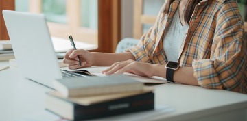 young women studying, taking notes and looking at laptop