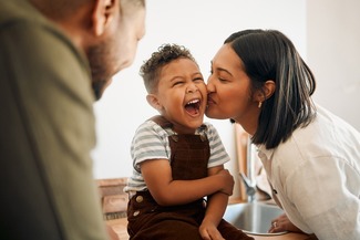 Happy boy getting a kiss by caring mother, bonding and laughing during family time at home.