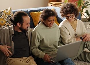 African American teenage girl using laptop together with her foster parents while they sitting on the floor in the room