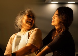 In the kitchen at home, a senior adult and their daughter cook together, sharing love and care. 