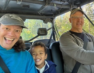 grandparents driving golf cart with child tucked in the middle smiling